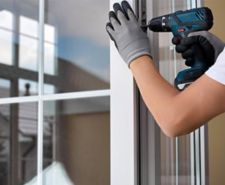 A man with gloves on screwing and adjusting the french door with a screwdriver