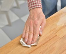 Man's hand applying oil to a wooden tabletop with a cloth.