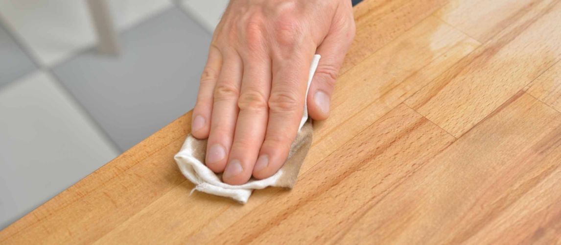 Man's hand applying oil to a wooden tabletop with a cloth.