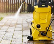A pressure washer with someone cleaning patio tiles behind