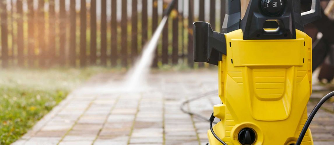 A pressure washer with someone cleaning patio tiles behind