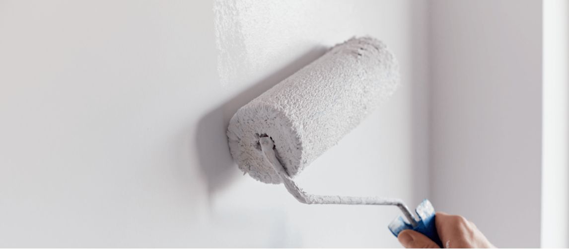 Man painting wall with white paint and a roller