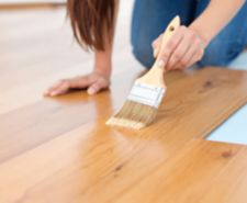 applying varnish to a wooden floor with a paintbrush.