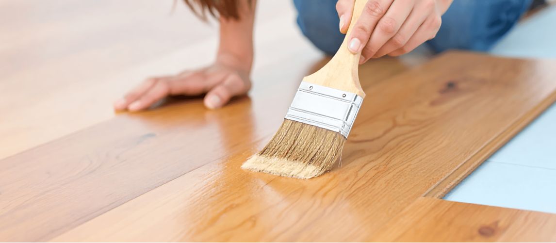 applying varnish to a wooden floor with a paintbrush.