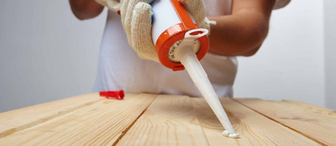 person using caulking gun to apply caulk to wood
