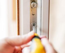 person using screwdriver to put screw into cylinder in door