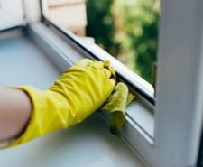 Person wearing a marigold glove cleaning a uPVC window frame