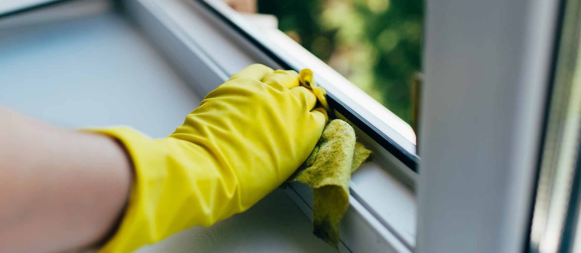 person wearing yellow glove wiping window sill frame