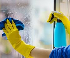 Person in yellow gloves cleaning a glass window with a blue cloth and spray bottle