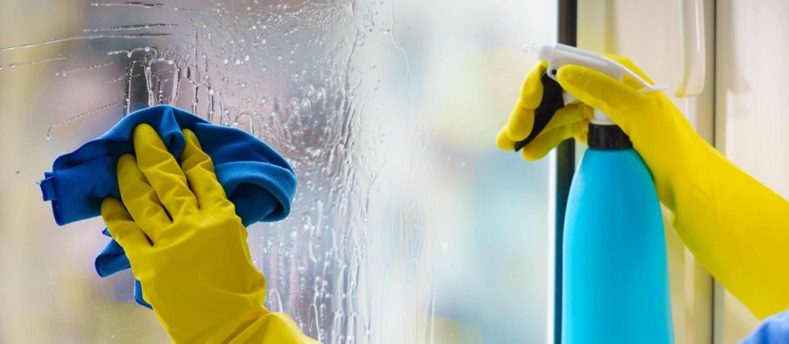 Person in yellow gloves cleaning a glass window with a blue cloth and spray bottle