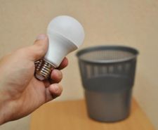 Hand holding a light bulb over an open bin
