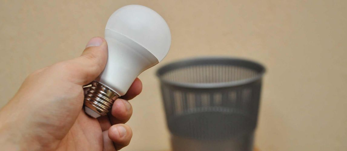 Hand holding a light bulb over an open bin