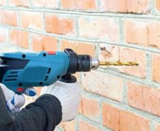 A person holding a percussion drill with a masonry bit in against a brick wall ready to drill a hole into brick