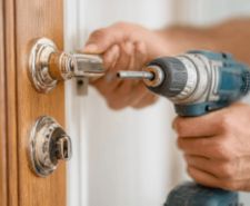 A person works on a door lock with a power drill.