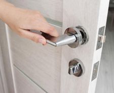 A man's hand opens an interior door with a broken doorhandle.