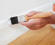 Painter brushing white paint onto a skirting board