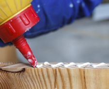 close up of glue nozzle applying glue onto wood