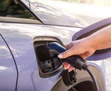 Female hand inserting an electric charging plug into a purple electric car