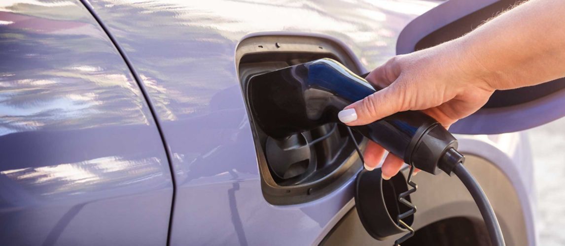 Female hand inserting an electric charging plug into a purple electric car