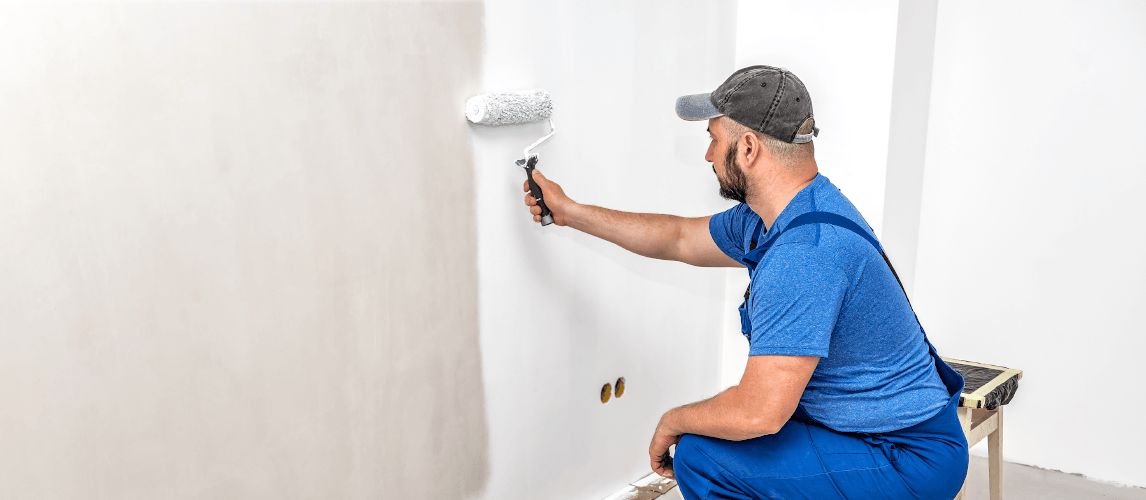 man using a paint roller to paint a wall white