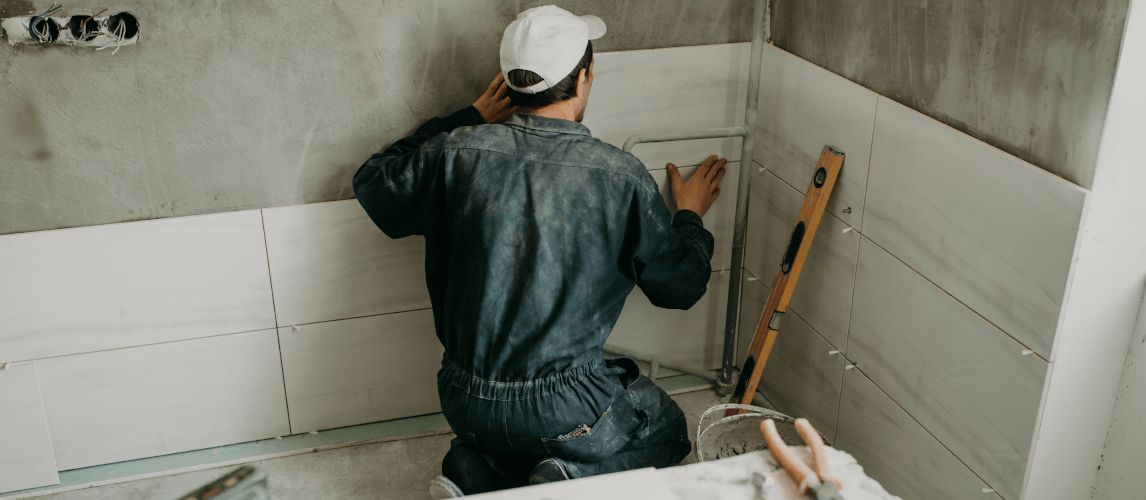 Worker repairman puts large ceramic tiles on the walls in the room