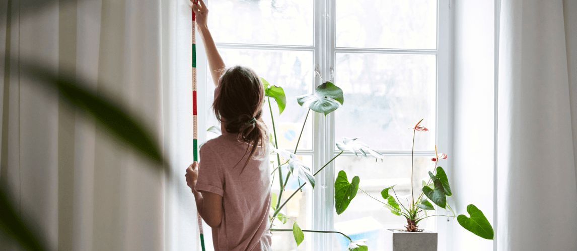 Rear view of a woman measuring curtains on wall at home