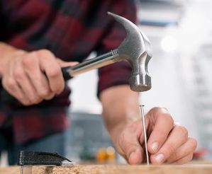 Person holding a hammer about to strike a nail into a piece of wood
