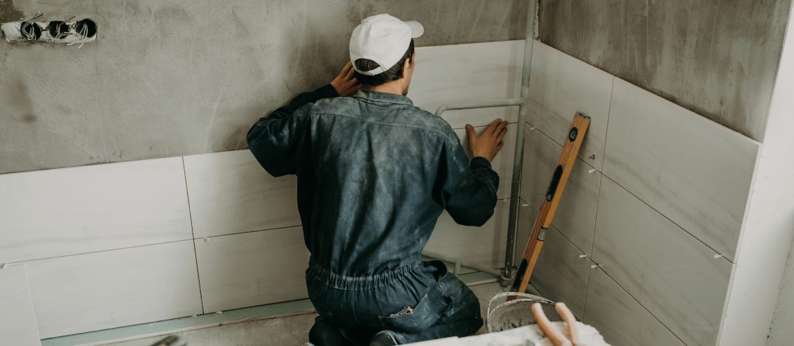 Worker repairman puts large ceramic tiles on the walls in the room