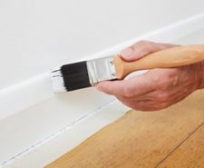 Painter brushing white paint onto a skirting board