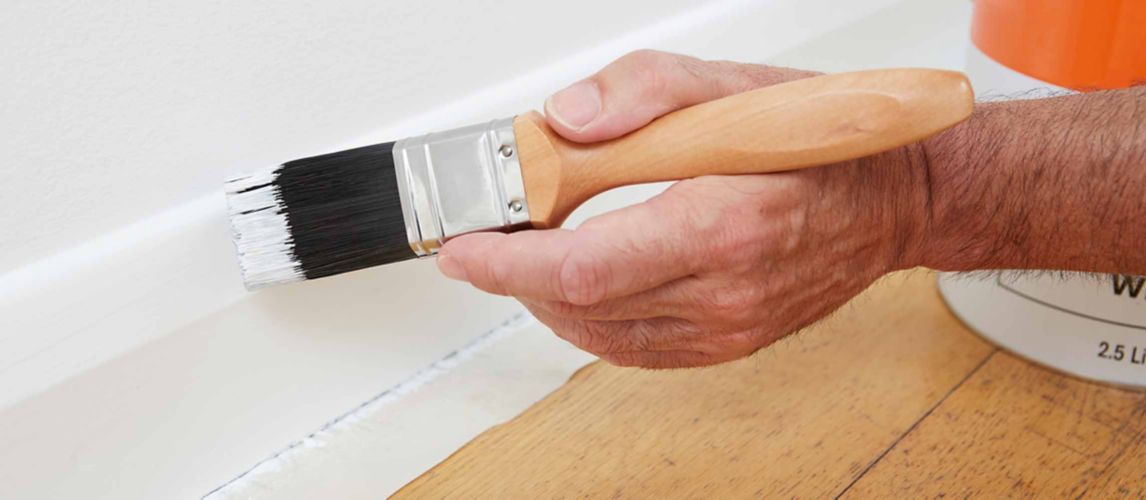 Painter brushing white paint onto a skirting board