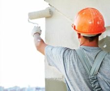 Man using a paint roller to apply white paint on a plastered wall
