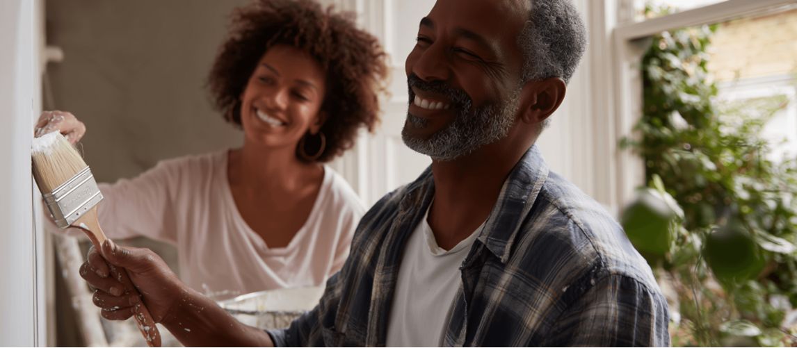 Man and woman smiling as they paint a wall together