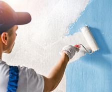 man painting a blue wall with white paint using a roller