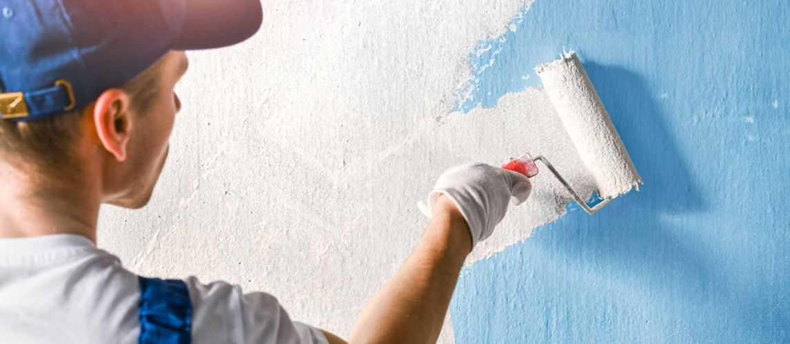 man painting a blue wall with white paint using a roller