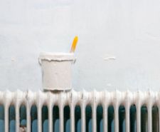 paint pot and paintbrush on a radiator in front of painted wall