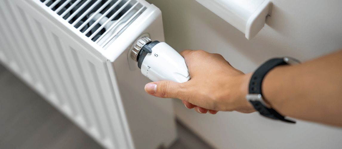 A woman's hand turning the heating knob on a radiator