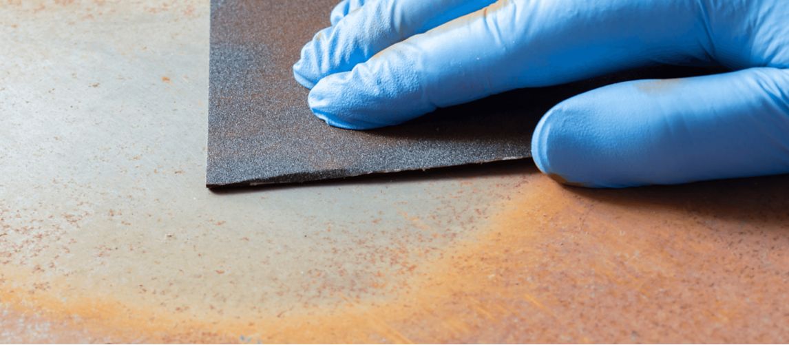 close up of hand wearing blue gloves cleaning rust from a steel object