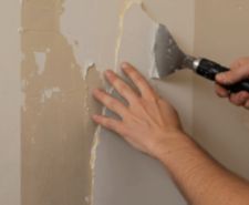 Close-up of hands using a steam scraper to remove old peeling wallpaper