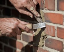 Super close-up shot of a worker scraping old mortar out of a brick wall joint. A detailed image for masonry repair, renovation, and building restoration.