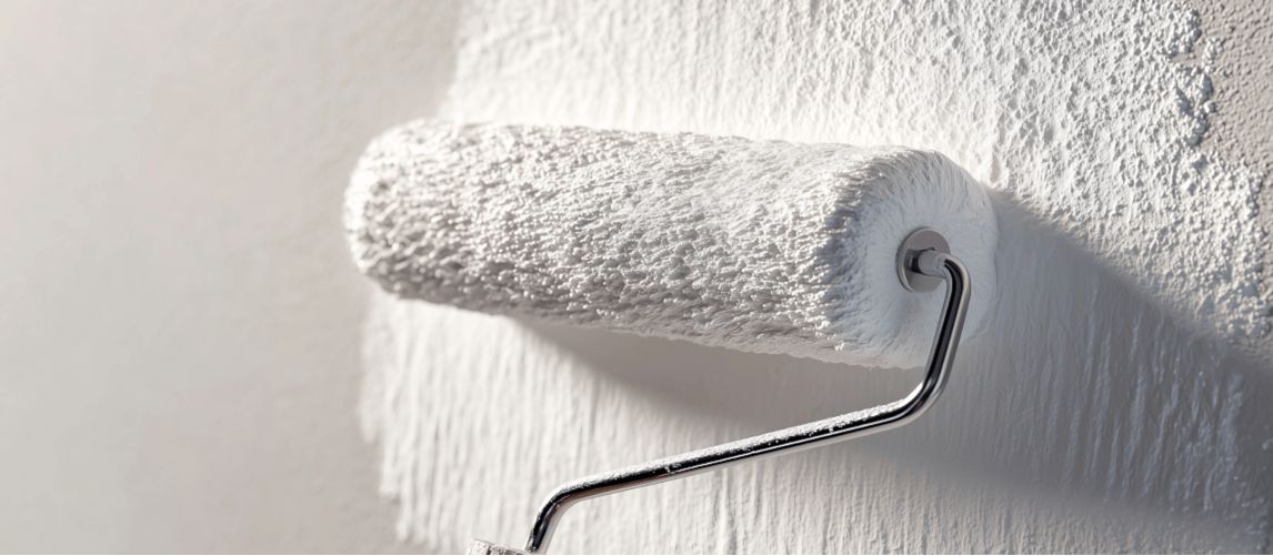 roller painting white paint onto plastered wall