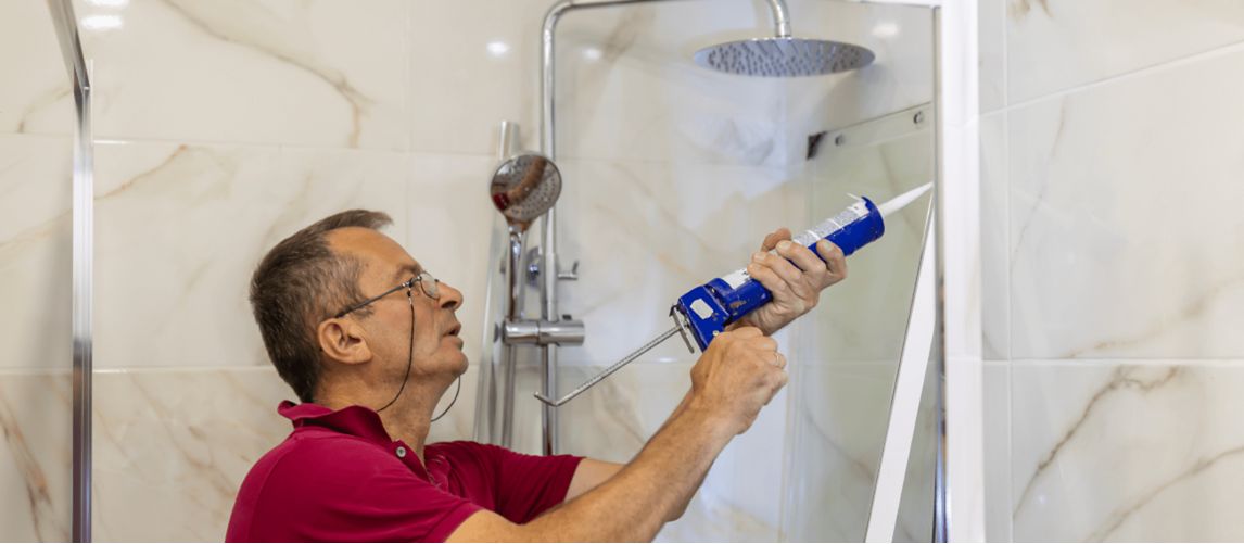 man using silicone sealant to seal shower frame