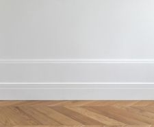 White skirting board installed on a white wall above a wood herringbone effect floor