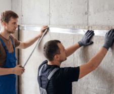 Two workers fitting acoustic insulation panels to a wall.