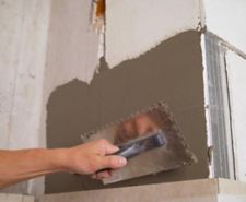 Person applying plaster over plasterboard with a trowel.