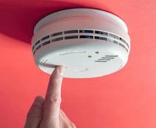 Finger pressing button on the face of a domestic fire alarm