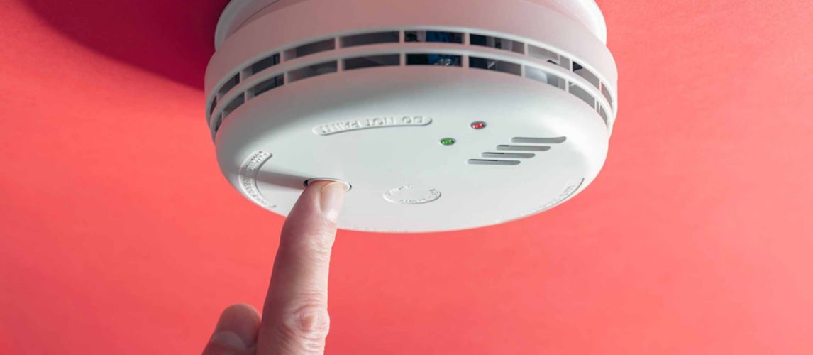 Finger pressing button on the face of a domestic fire alarm