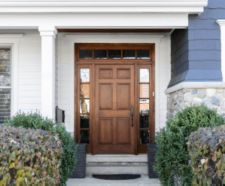 A wooden front door, surrounded by windows, with white, blue, and stone siding.