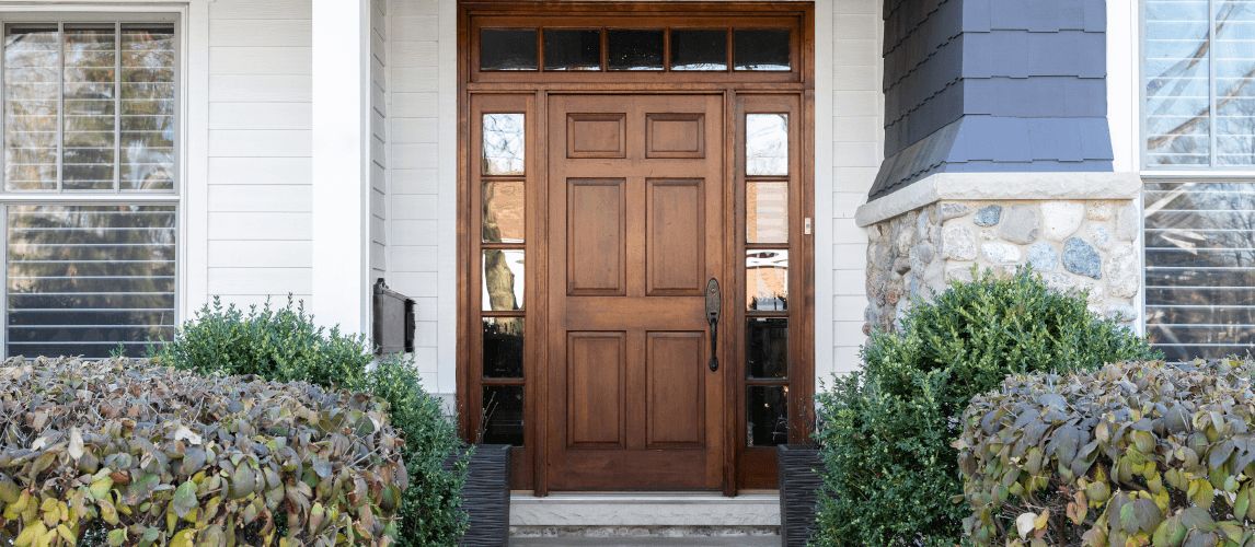 A wooden front door, surrounded by windows, with white, blue, and stone siding.
