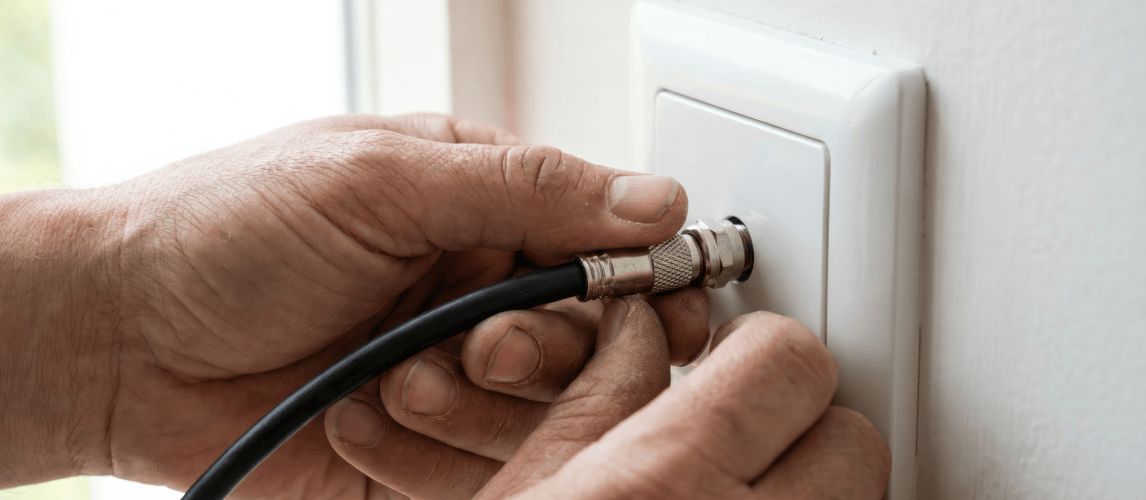 Hands connecting a black coaxial antenna cable to a white wall outlet socket