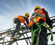 Two construction workers in protective gear working at height on a steel structure.